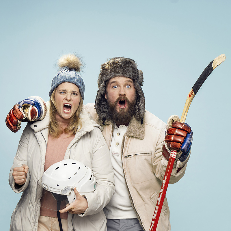 Två personer klädda i vinterkläder som ser ut att heja på en match. Till vänster Stina Nordberg hållandes en hockeyhjälm, till höger Philip Lithner hållandes en hockeyklubba.